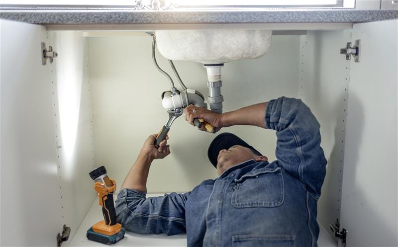Plumber repairing pipes beneath a bathroom sink in Jurupa Valley