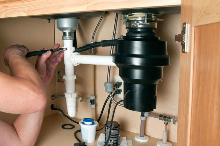 Plumber installing a garbage disposal beneath a kitchen sink in Jurupa Valley
