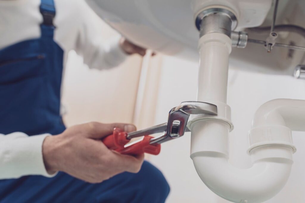 Plumber repairing a white drain pipe beneath a sink in Jurupa Valley