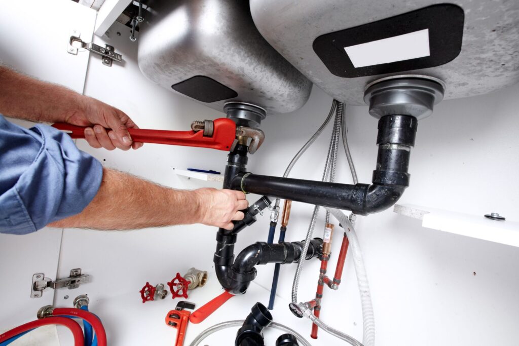 Plumber repairing drain pipes beneath a kitchen sink in Jurupa Valley